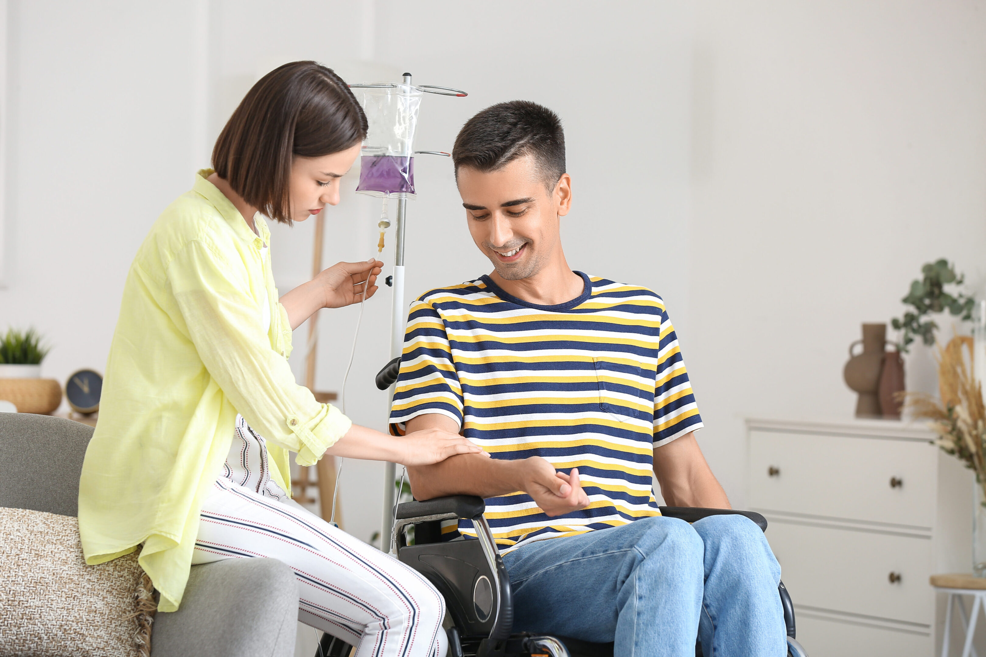 Young woman and her husband in wheelchair undergoing medical rehabilitation at home